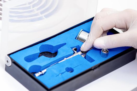 Human hand in protective glove taking out airbrush tool for painting nails from the box in salon
