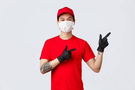 Click this button, download delivery app. Asian courier in red uniform cap and t-shirt, wearing protective mask, medical gloves, pointing fingers right, invite try promo, introduce special offer.