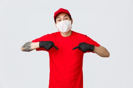 In time delivery with this company couriers service. Cheerful asian courier in cap and red t-shirt, wearing medical mask and gloves to protect customers from covid19 virus spread, pointing himself.