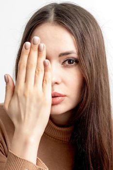 Portrait of beautiful young caucasian woman covering her half face with her hand on white background
