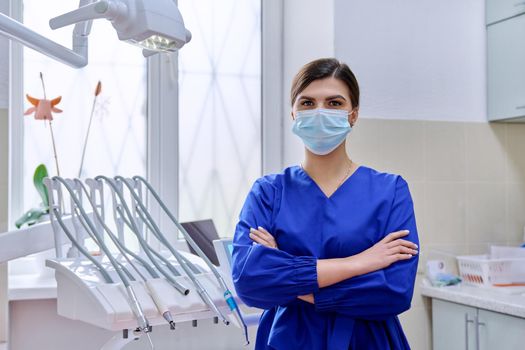 Portrait of confident female dentist doctor in office looking at camera. Young female in medical protective mask in blue uniform, copy space. Dentistry, medicine, health care, profession, stomatology