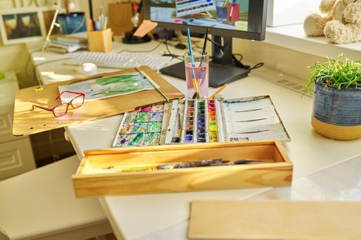 Drawing, artwork, hobby, education, creativity concept. Close-up of watercolor drawing, glasses, watercolor paints in box, brushes on the table, nobody