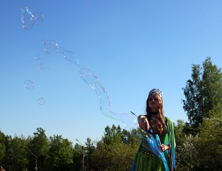 A beautiful girl in a butterfly costume and a crown blows soap bubbles. Carnival..