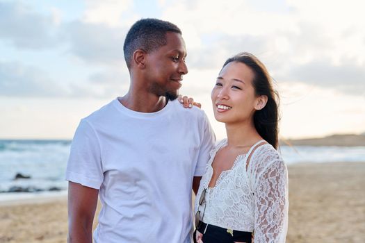 Young couple in love on the beach together. Multiethnic couple, asian woman and african american man. Love, honeymoon, relationship, lifestyle, togetherness, happiness, dating, multicultural family concept