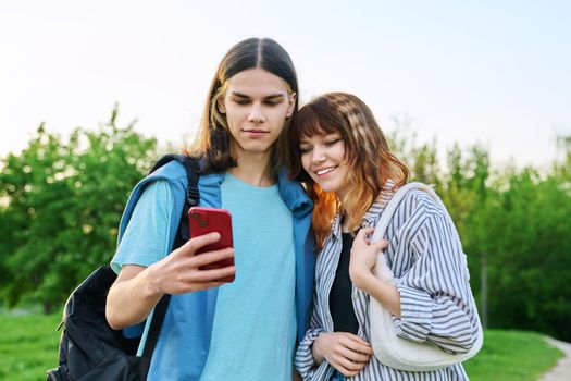 Couple of college students friends looking at smartphone screen outdoor. Beautiful fashionable guy and girl 17, 18 years old together. Friendship, lifestyle, youth concept