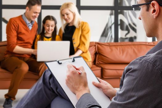 Hand of a professional family psychotherapist writing notes in front of a family with a child during a consultation.