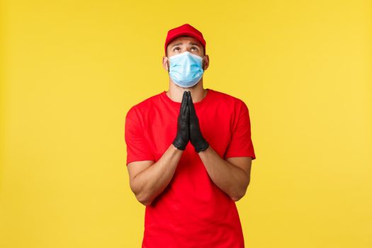 Express delivery during pandemic, covid-19, safe shipping, online shopping concept. Courier with hope, pleading God end coronavirus infection, press hands in pray, look up, wear face mask.