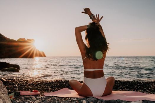 Young woman in swimsuit with long hair practicing stretching outdoors on yoga mat by the sea on a sunny day. Women's yoga fitness pilates routine. Healthy lifestyle, harmony and meditation concept.