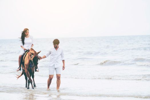 Young couple goes honeymoon horse riding on the beach in summer vacation.