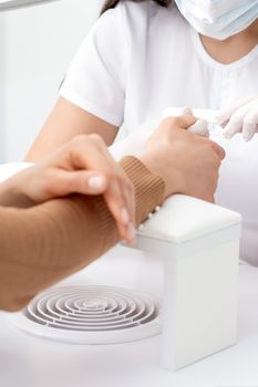 Young woman receiving a manicure by a beautician with nail file in a nail salon. Manicurist filing client's nails