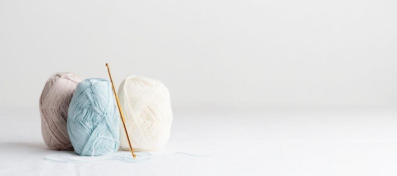 Needlework. Crochet hook and balls of cotton yarn pastel colors on a white table, copy space