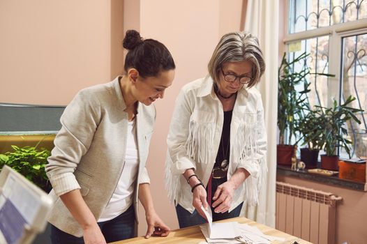 Mature Caucasian woman senior fashion designer and her colleague tailor working with pattern in a fashion clothing design and tailoring atelier, creating new collection of clothes. Fashion design