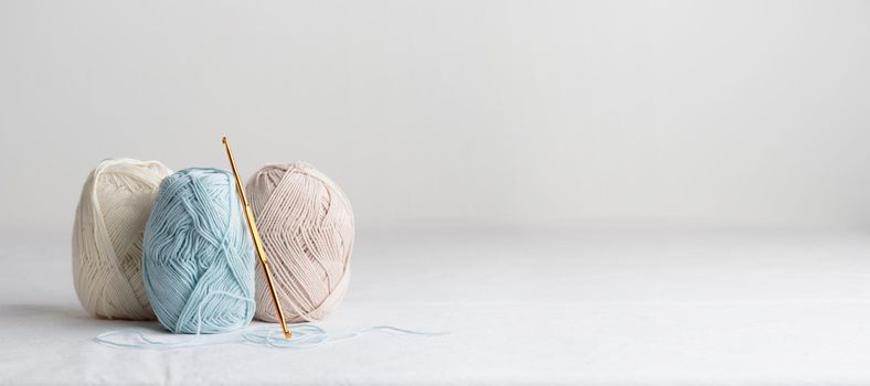 Needlework. Crochet hook and balls of cotton yarn pastel colors on a white table, copy space