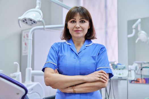 Portrait of smiling nurse looking at camera in dentistry. Confident female with folded hands, dental clinic equipment background. Dentistry, medicine, health care, profession, stomatology concept
