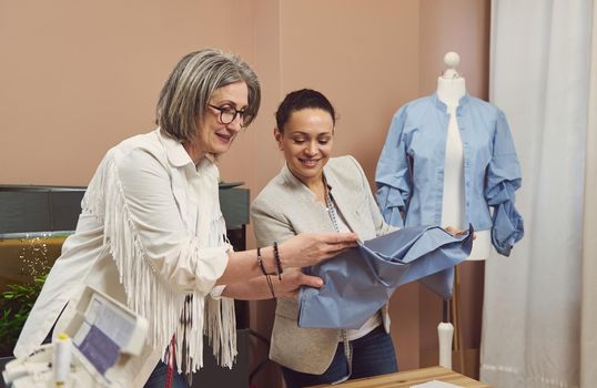 Two seamstresses at work. Skilled fashion designers tailors dressmakers looking at fabric, discussing quality of textile. Colleagues at modern sewing atelier improving production process together