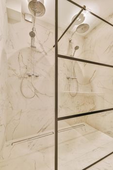 Shower faucets attached to tiled wall near glass partition and ornamental curtail in washroom at home