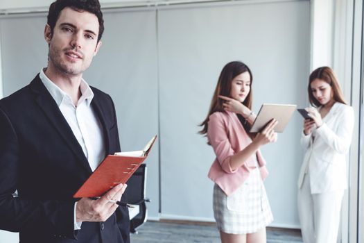 Happy young handsome businessman reading book and working in office with colleagues and friend at workplace. Corporate business people group.