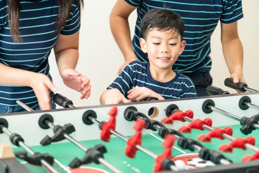 Happy kid playing foosball table soccer with family, father and mother.