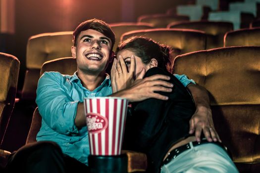 A couple of caucasian watch a thriller movie in the cinema, woman eyes closed and turning her face away from the screen