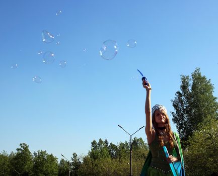 A beautiful girl in a butterfly costume and a crown blows soap bubbles. Carnival..