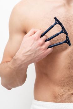 Young caucasian man with beard holds razor shaves his chest with white shaving foam on white background. Man shaving his torso