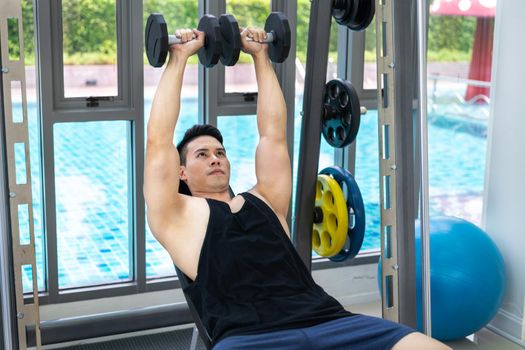 Muscular man bodybuilder in fitness gym training with dumbbells. Healthy lifestyle and bodybuilding concept.