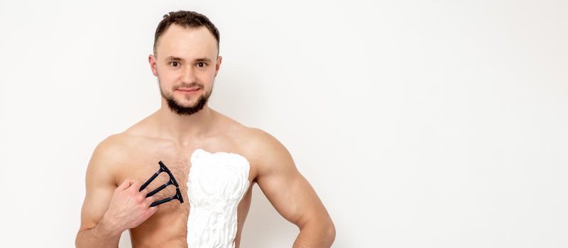 Young caucasian man with beard holds razor shaves his chest with white shaving foam on white background. Man shaving his torso