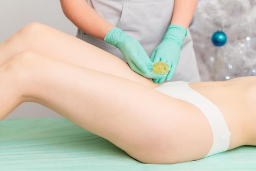 Beautician waxing female legs in spa center.