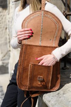 Woman with a brown leather backpack with antique and retro look. Outdoors photo.