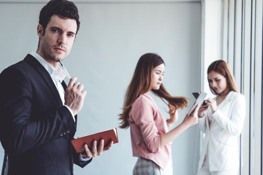 Happy young handsome businessman reading book and working in office with colleagues and friend at workplace. Corporate business people group.