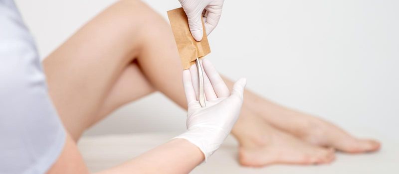 Human hands in protective gloves taking off medical or beauty tools from craft envelope before procedures on background of female legs