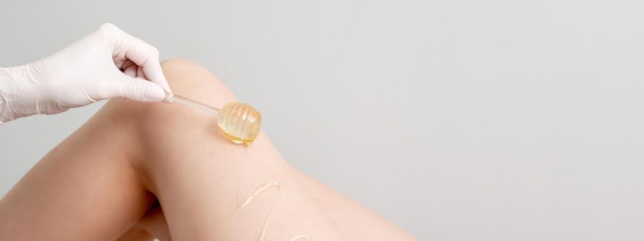 Wax on honey stick flowing down on female leg in human hand wearing protective glove on white background