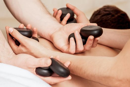 Young man receiving a stone massage on back while hands of massage therapist puts stones on her back.