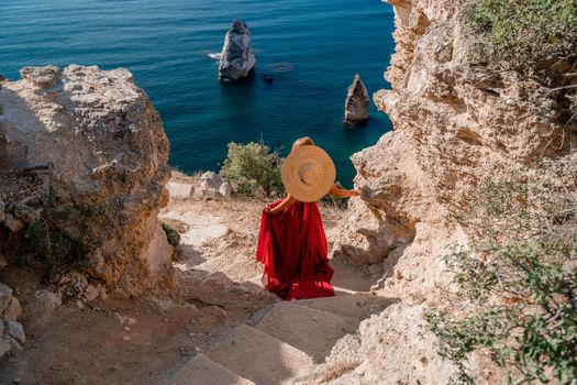 A woman in a flying red dress fluttering in the wind and a straw hat against the backdrop of the sea