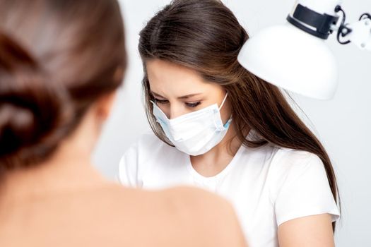 Manicurist wearing protective mask painting female nails with nail polish in manicure salon.