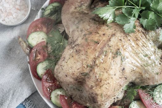 On the table on a plate of fried chicken with cucumbers, tomatoes and parsley. Top view, close-up