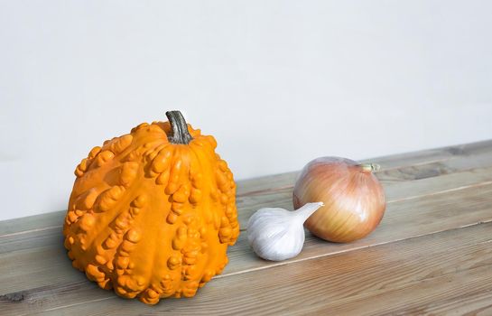 On the wooden table is a head of onion, garlic and orange pumpkin
