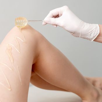 Wax on honey stick flowing down on female leg in human hand wearing protective glove on white background