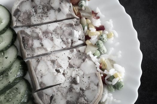 On the table on a plate of delicious meat appetizer: stuffed with meat and bacon pork stomach, sliced, next to vegetables and fresh cucumbers. Top view, close-up