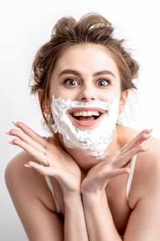 Beautiful young caucasian woman with shaving foam on her face posing on white background