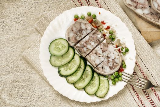 On the table on a plate of delicious meat appetizer: stuffed with meat and bacon pork stomach, sliced, next to vegetables and fresh cucumbers. Top view, copy space, flat lay