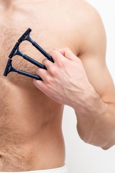 Young white man holds razor shaves on his chest on white background. Man shaving his torso