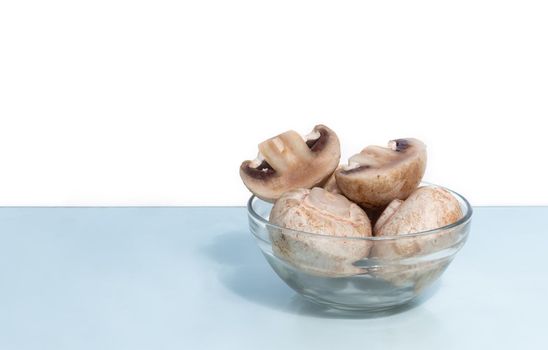 A few fresh raw mushrooms in a glass plate on a light background. Front view, copy space