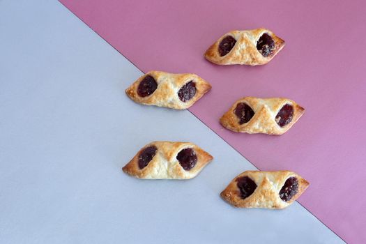 On a two-color background, delicious puff pastry cookies stuffed with raspberry jam. Top view with copy space. Flat lay