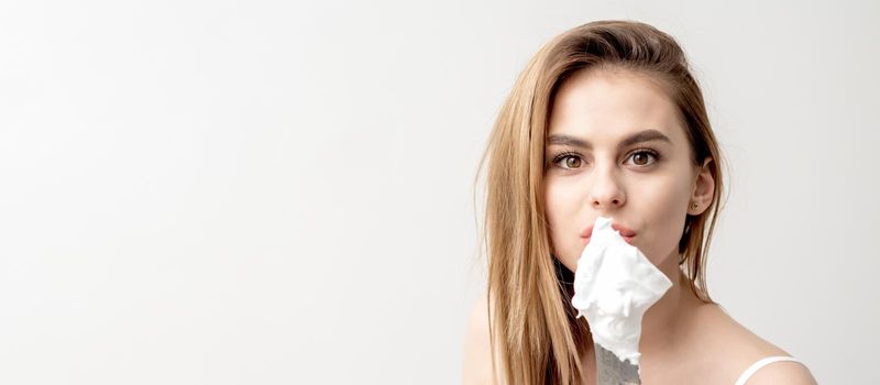 Portrait of young caucasian woman holding knife with shaving foam in front of her face on white background with copy space