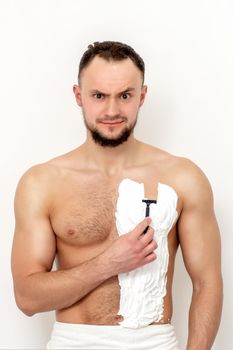 Young caucasian man with beard holds razor shaves his chest with white shaving foam on white background. Man shaving his torso