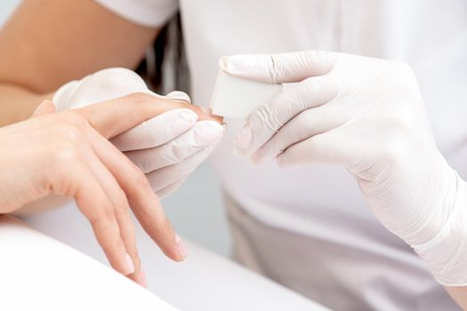 Close up of woman receiving manicure with nail file by manicurist at nail salon