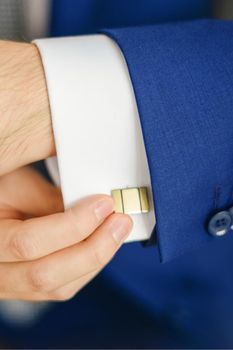 Groom or businessman fasten cufflink on the cuff of the shirt wearing blue suit