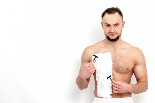 Young caucasian man with beard holds razor shaves his chest with white shaving foam on white background. Man shaving his torso