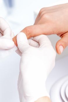 Manicure master removing nail polish with white cotton pad in beauty salon
